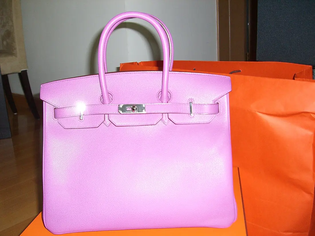 A pink Hermès Birkin handbag beside its orange box and packaging