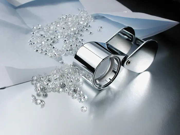 A parcel of small loose diamonds spilling from folded paper beside a jeweler's loupe