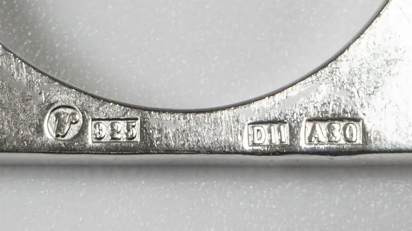 Macro photograph of stamps inside a silver ring: a maker's mark, the number 925, and two code stamps