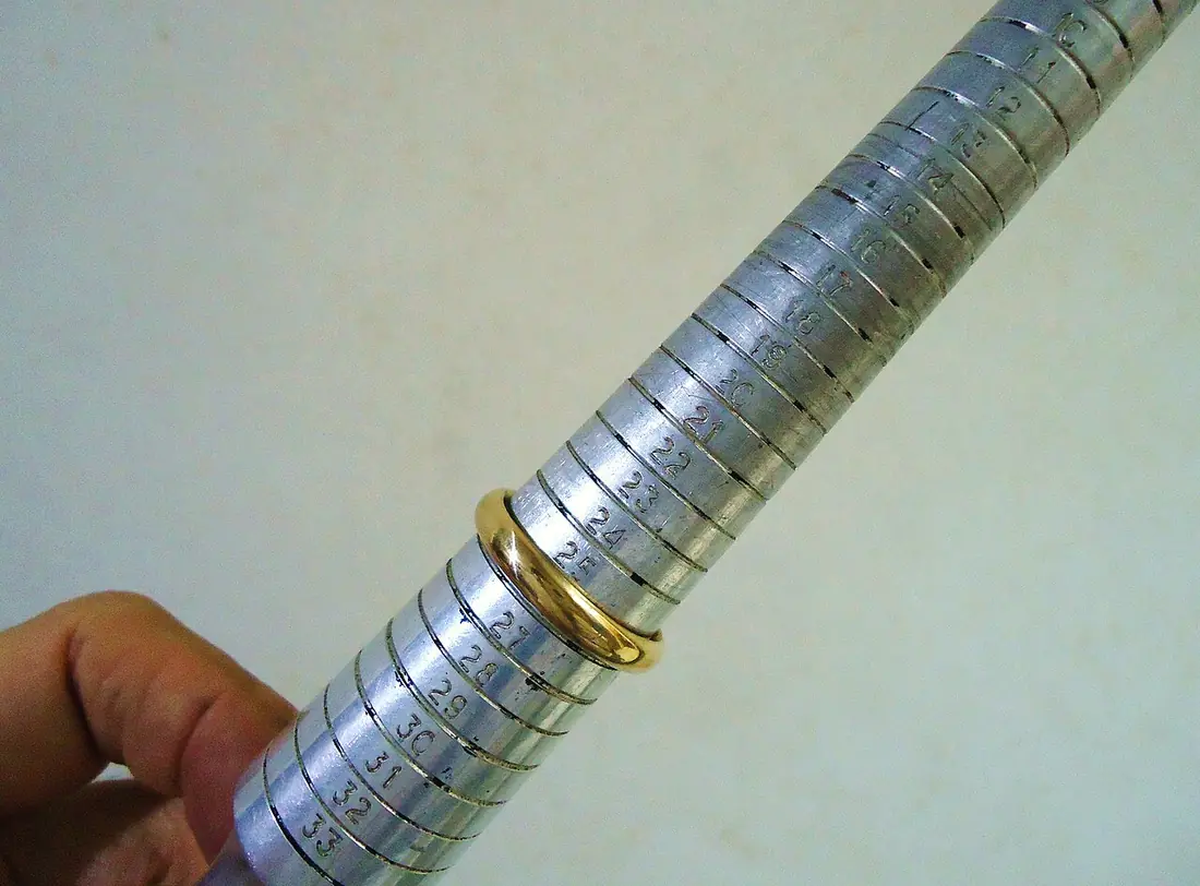 A gold wedding band on a numbered steel ring-sizing mandrel