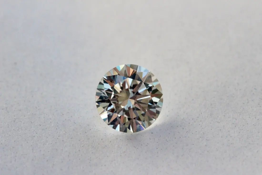 A loose round brilliant cut diamond photographed face-up on a grey surface