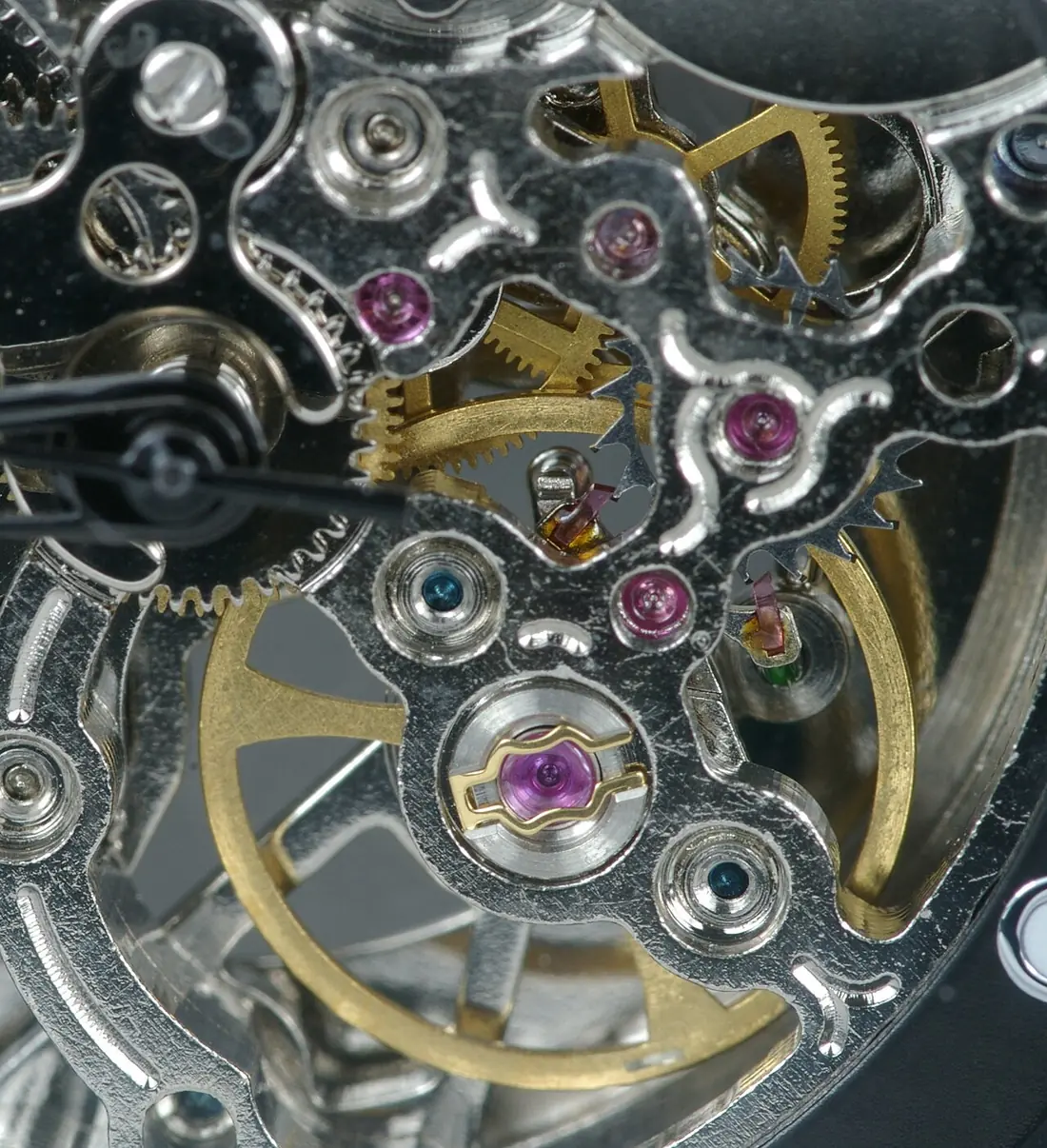 Macro photograph of a skeleton watch movement showing the balance wheel, pallet fork, escape wheel and ruby jewels