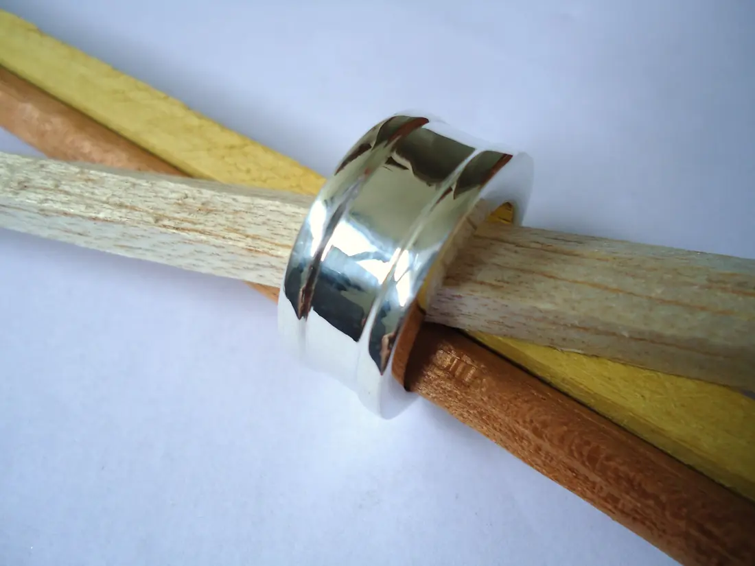 A wide, mirror-polished 18 carat white gold band resting on wooden dowels